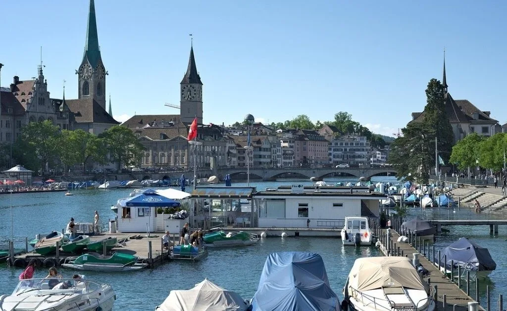 Aerial view of Zürich city with the Limmat River flowing through, surrounded by historic buildings, bridges, and boats on the water.