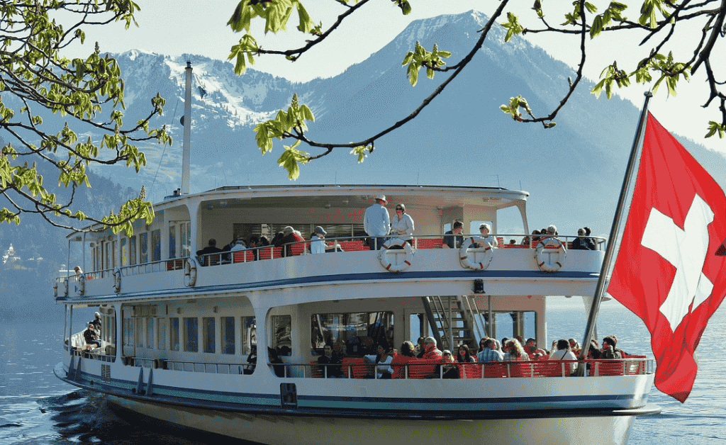 Scenic lake cruise on Lake Lucerne, Switzerland, with a Swiss flag waving in the foreground and mountains in the background.
