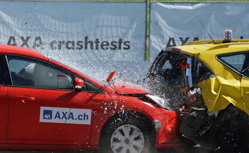 High speed photograph shows the collision of a red and yellow car during an AXA crash test, the shattered glass indicating impact.