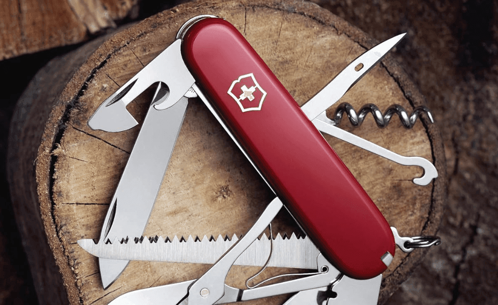 Red Swiss Army Knife with multiple tools displayed, resting on a log of wood.