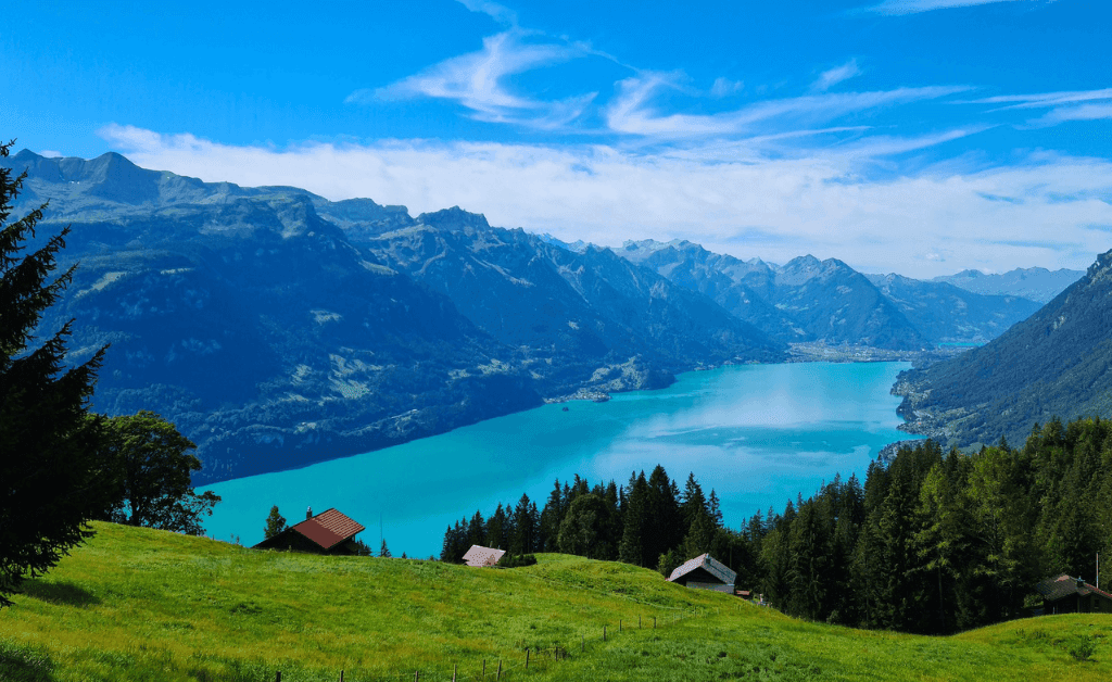 Scenic view overlooking Lake Thun in Switzerland, showing the turquoise water, rolling green hills, and the majestic mountains in the background.