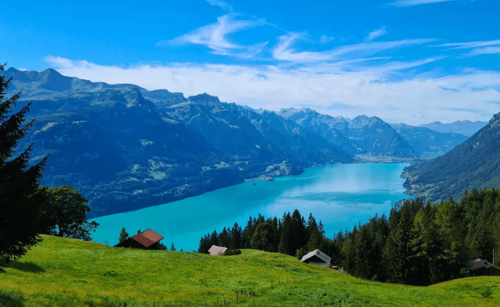 Scenic view overlooking Lake Thun in Switzerland, showing the turquoise water, rolling green hills, and the majestic mountains in the background.