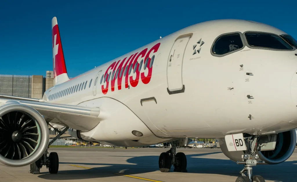Airbus A220 in SWISS livery sits parked at an airport terminal with the Star Alliance logo visible.