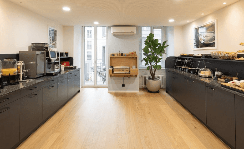 Clean and modern breakfast buffet setup at Fred Hotels Zürich featuring coffee machines, juice, pastries, and a toaster station.