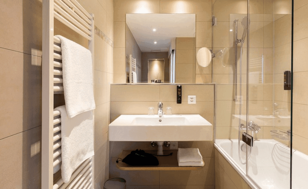 Modern, clean bathroom at Fred Hotels Zürich with a tub/shower, heated towel rack, wall-mounted vanity, and large mirror.