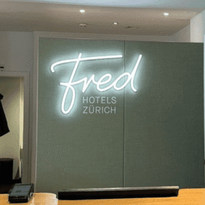 Reception desk at Fred Hotels Zürich featuring a modern white neon script sign on a light green wall.