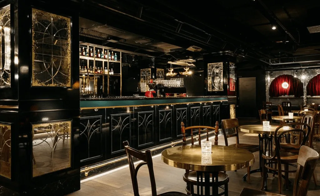 Interior of the Ruby Mimi Hotel’s 24-hour bar in Zürich with black lacquer, brass accents, round tables, and vintage cinema lighting.
