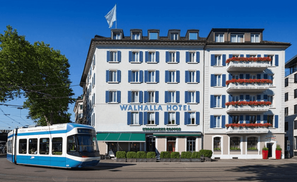 Exterior of the Walhalla Hotel Zürich near the main train station with a blue tram passing in the foreground.